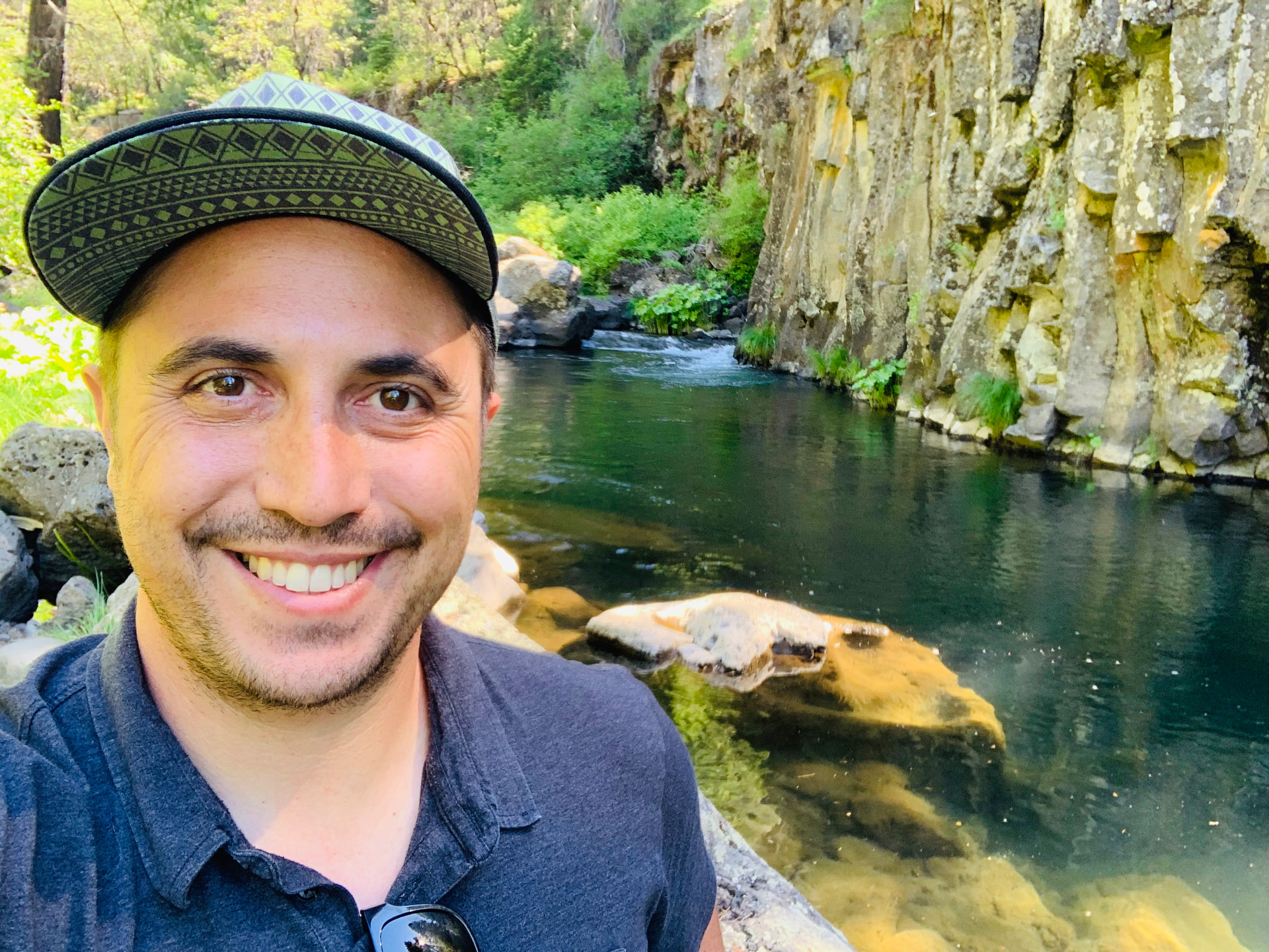 Ryan Conklin smiling beside a river surrounded by trees and rock cliffs